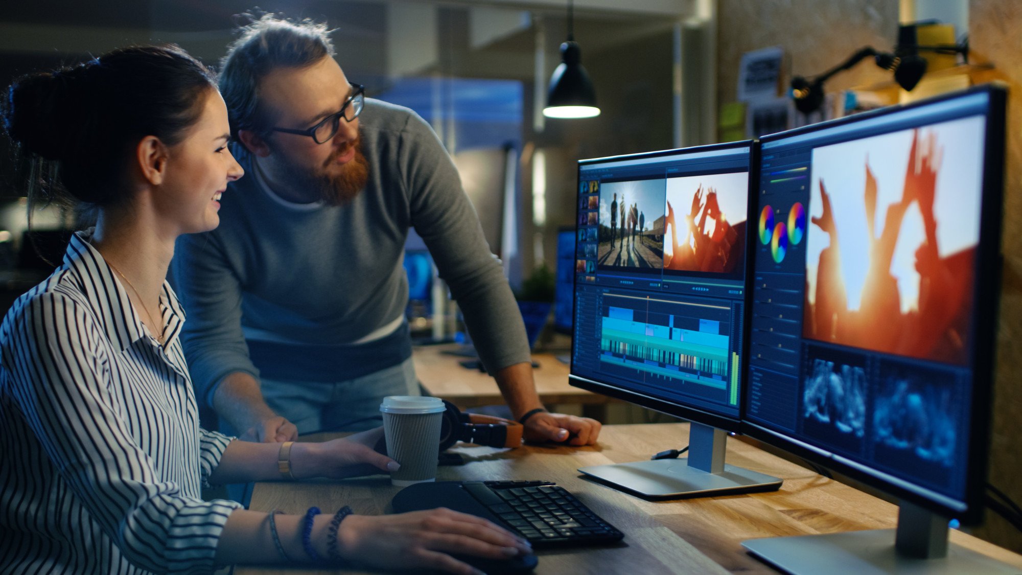female video and sound editor works with her male colleague on a project on her personal computer with two displays. they work in a creative loft office.